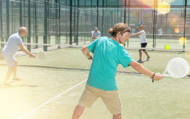 Adult man and elderly man doubles playing against two men in padel tennis on court