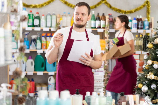 Young man seller with woman assistant conducting inventory in household chemicals store decorated for christmas