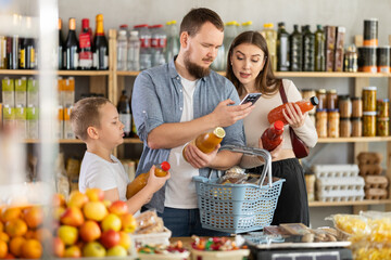 Couple young man and woman with son scanning qr code of natural juices with phone in grocery store..
