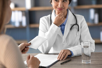 A young Indian woman in a white coat smiles while receiving payment from a patient. The setting is a clinic office, emphasizing a scene of potential corruption and unethical practices.