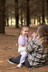 Mother and daughter playing patty-cake together while sitting in a pine forest.