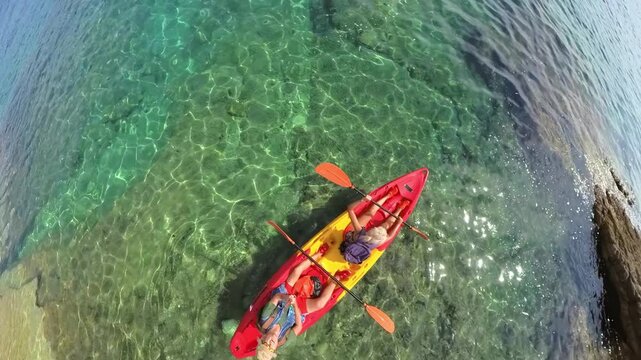 People enjoying a summer vacation, paddling a tandem kayak on the crystal clear turquoise water near the rocky coast of Cape Kamenjak Natural Park in Croatia