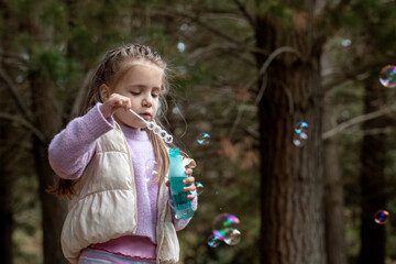 Cute little girl blowing soap bubbles while spending time in the park.