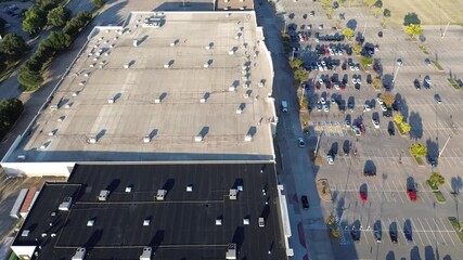 Large Lewisville shopping complex shows dual roof sections light and asphalt-based, lined with HVAC units, facade parking with EVs, handicapped zones, and tree buffer casting morning shadows