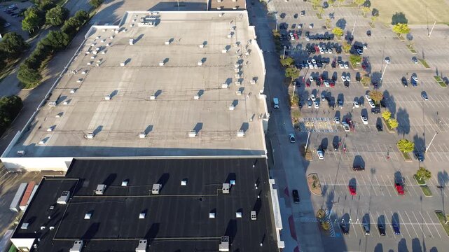 Large Lewisville shopping complex shows dual roof sections light and asphalt-based, lined with HVAC units, facade parking with EVs, handicapped zones, and tree buffer casting morning shadows