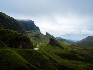 A breathtaking view of lush green hills with dramatic rocky formations under a cloudy sky showcases the beauty of a remote valley. Generative AI.