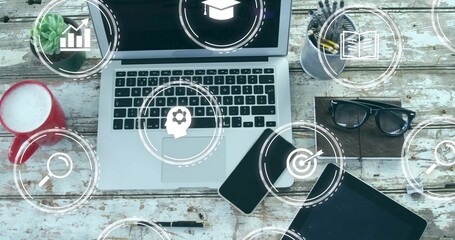 Presenting laptop showing digital overlay icons at study desk with coffee mug, gadgets, accessories