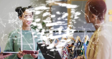 Discussing designer holding pink notebook with pencil by clothing rack in design studio, copy space