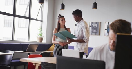 Male and female coworkers wearing business attire reviewing teal binder in coworking office