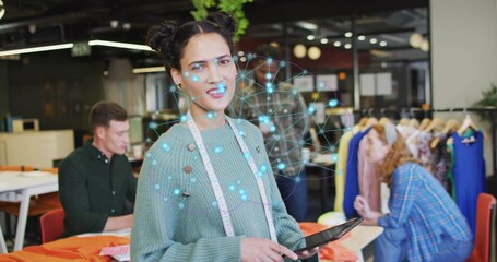 Holding tablet, female designer directing colleague handling orange fabric in open-plan studio