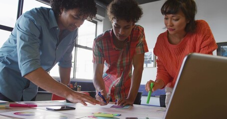 Collaborating three coworkers analyzing printed charts at meeting table, with laptop sticky notes