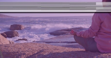 Sitting woman wearing pullover hoodie and leggings meditating on rock at rocky shore, copy space