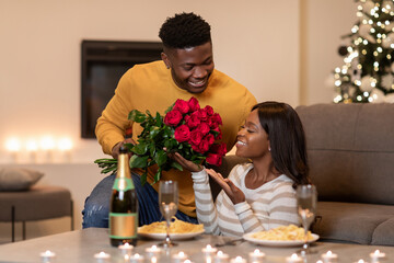 A joyful African man presents a bouquet of red roses to his girlfriend as they celebrate...