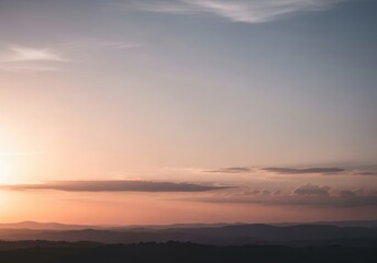 Fototapeta premium Soft pastel colors of a serene sunset sky over distant mountains