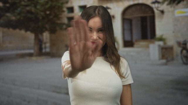 Woman waving hand on a stone street in front of a building entrance, smiling and offering a greeting; warmth.