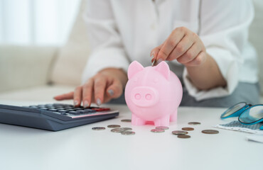 Person saving money inserting coin into pink piggy bank while calculating budget, personal finance, budgeting and financial planning at home with calculator, financial goal management, cost control