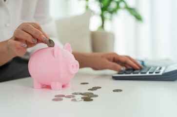 Person saving money inserting coin into pink piggy bank while calculating budget, personal finance, budgeting and financial planning at home with calculator, financial goal management, cost control