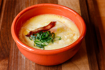 Delicious bowl of creamy soup garnished with crispy bacon and green onions on a wooden table