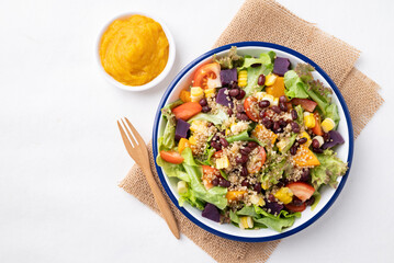 Healthy vegetable salad with lettuce, quinoa seed, azuki bean, corn, tomato, pumpkin and purple sweet potato in a bowl and pumpkin dressing. Vegan and plant-based food