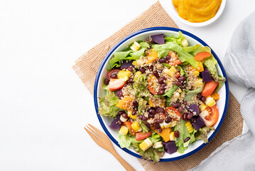 Healthy vegetable salad with lettuce, quinoa seed, azuki bean, corn, tomato, pumpkin and purple sweet potato in a bowl and pumpkin dressing. Vegan and plant-based food