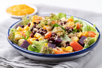 Healthy vegetable salad with lettuce, quinoa seed, azuki bean, corn, tomato, pumpkin and purple sweet potato in a bowl and pumpkin dressing. Vegan and plant-based food