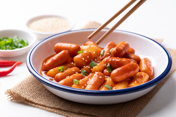 Korean Tteokbokki (simmered rice cake) and sausage with spicy sauce in bowl with chopsticks