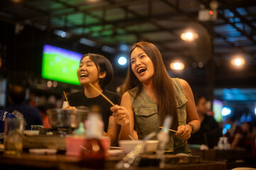 Asian friends enjoying hot pot with skewers at night restaurant
