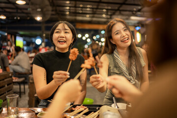 Asian friends eating street food skewers at night market