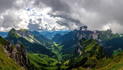 Obraz premium Panoramic view of a lush green mountain valley under dramatic stormy clouds with sunlight breaking through illuminating the rugged peaks and distant landscape on a summer day