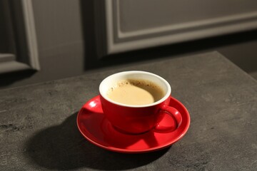 Red cup of aromatic coffee and saucer on dark textured table