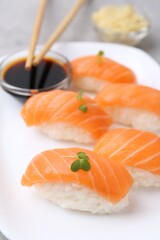 Delicious nigiri sushi with salmon, microgreens and soy sauce on grey table, closeup