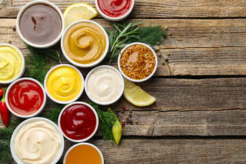 Different sauces in bowls and ingredients on wooden table, flat lay. Space for text