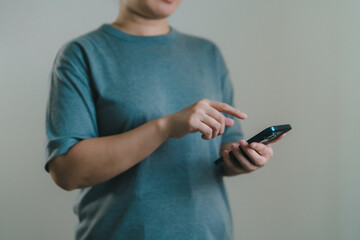 Woman in a casual blue t-shirt is using a smartphone, tapping the screen with one hand Concept of digital lifestyle, mobile communication, social media interaction, and modern technology in life.