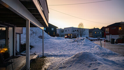 A quiet residential neighborhood in city of Tromsø, Norway with houses. Roads are covered in deep winter snow during a soft pastel sunset.