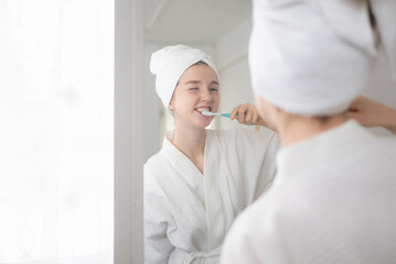 A young woman stands in front of a mirror, brushing her teeth