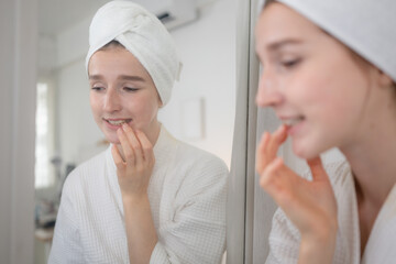 A young woman stands in front of a mirror, brushing her teeth
