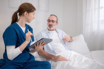 Female nurse assisting an elderly patient in bed while reviewing medical information
