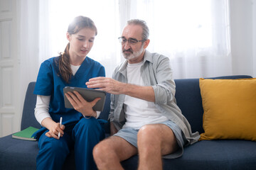 Fototapeta premium A female nurse assists an elderly patient in couch of living room with explain medication