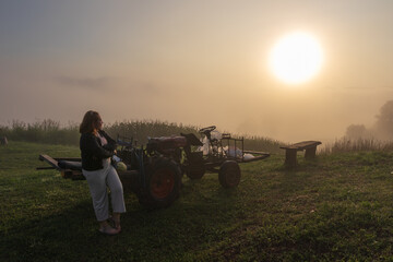 Obraz premium Woman Leaning on Tractor in Misty Field