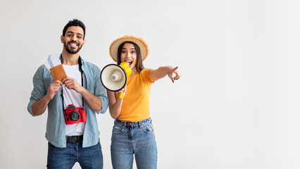 Two happy travelers stand together, holding travel tickets and a megaphone. They are excited and...