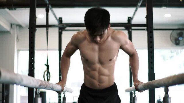 Muscular man dips in gym, exercising on parallel bars; health and fitness concept