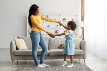 A mother and her young daughter engage in a joyful dance in their inviting living room. Soft sunlight filters through large windows as they share laughter and smiles.