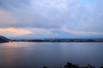 Lakeside Cityscape at Sunrise with Bridge and Mountain Backdrop Beneath Dramatic Cloud Cover