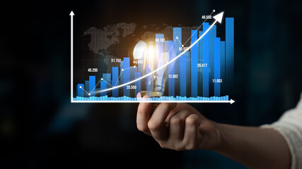 A hand holding a light bulb symbolizes innovative ideas while an upward financial graph represents...