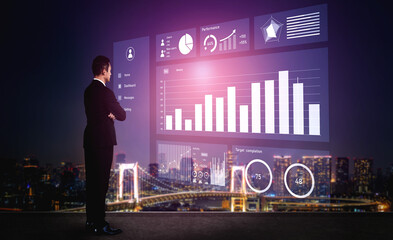 A businessman stands before a transparent digital screen showcasing data visualizations against a stunning night cityscape, highlighting performance metrics. Impute