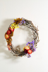 Autumn grapevine wreath with dried flowers, yellow, red, and purple blooms on white wall
