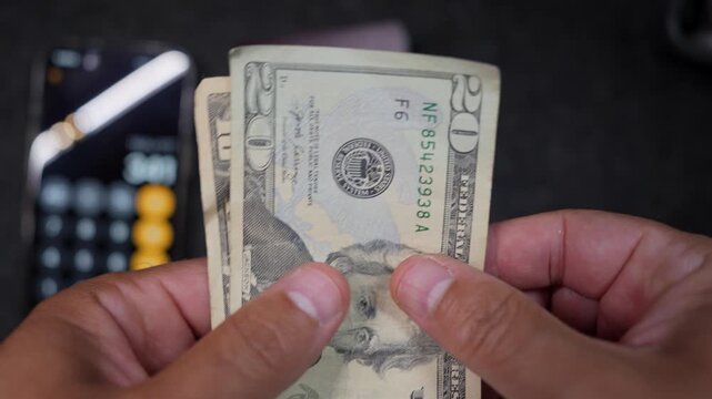 Close-up shot of hands counting crisp US dollar bills, focusing on the texture and detail with soft lighting and a blurred background, evoking themes of finance and economy.