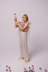 Young caucasian girl, blonde hair, pink festive top, sequin pants, white shoes, side view, holding...
