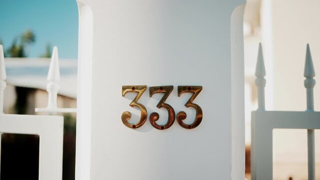 Golden metallic number 333 mounted on a white wall in sunlight