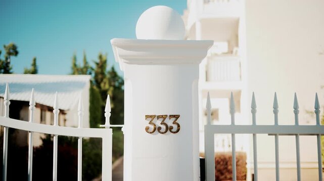 Golden metallic number 333 mounted on a white wall in sunlight